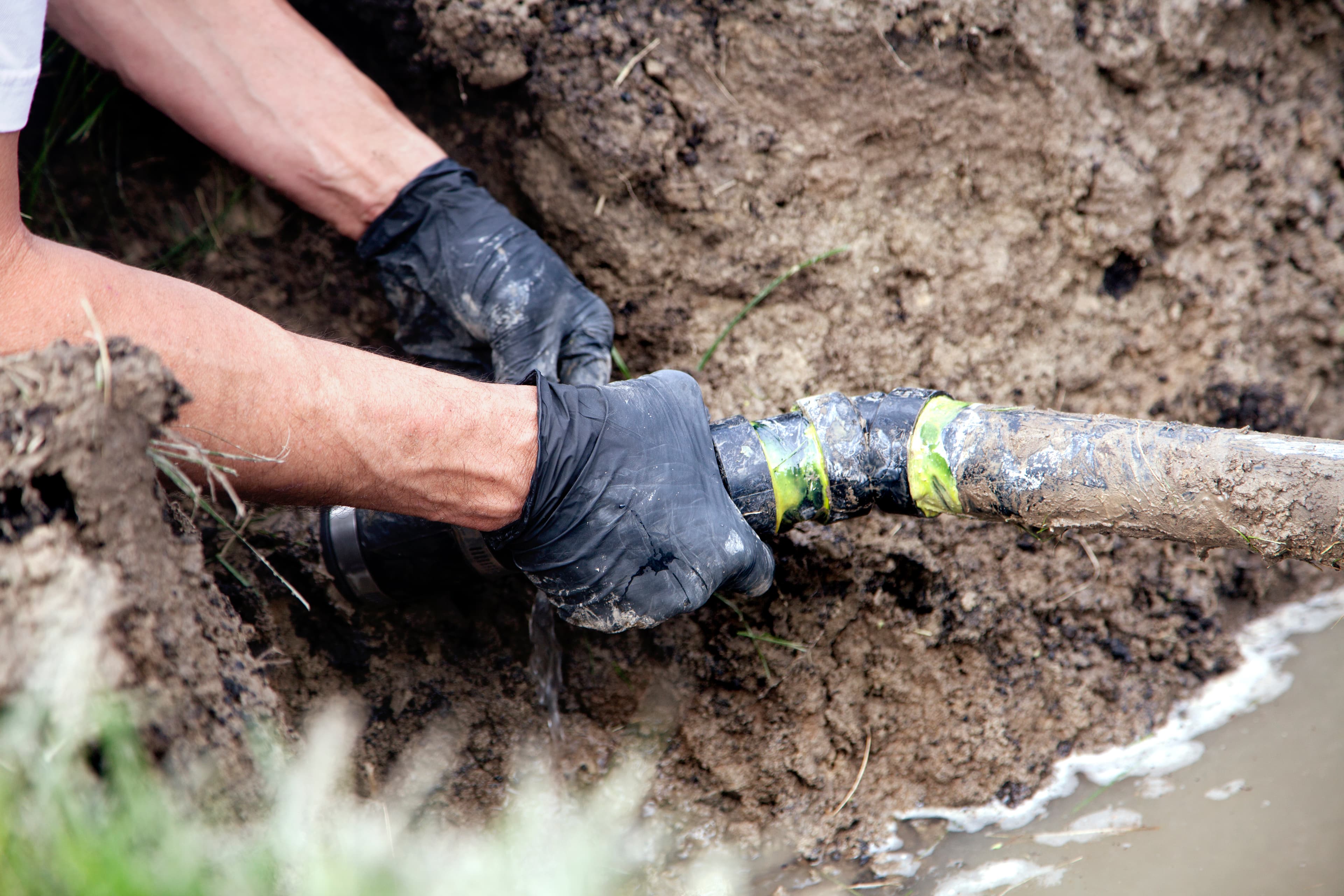 Gloved hands joining pipe in a muddy trench